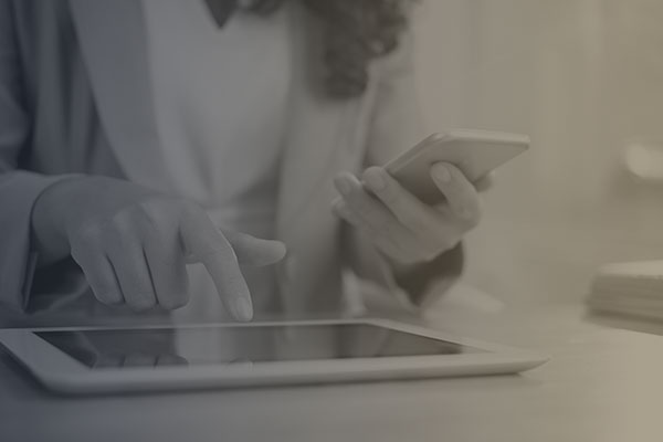 A woman using an tablet on a table while looking at a phone working on commercial IT for the US government