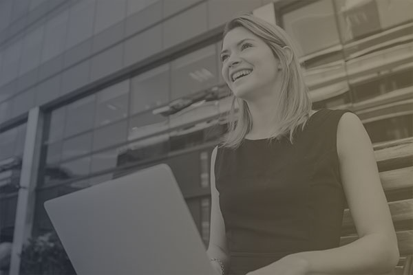 A woman with her laptop in front of an office building representing Allyon as a certified Women Owned business